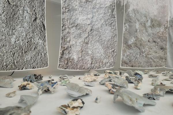 Photograph of a display in Manningham Art Gallery's Curio window space featuring amorphous ceramic items in the foreground and silk prints in the background.