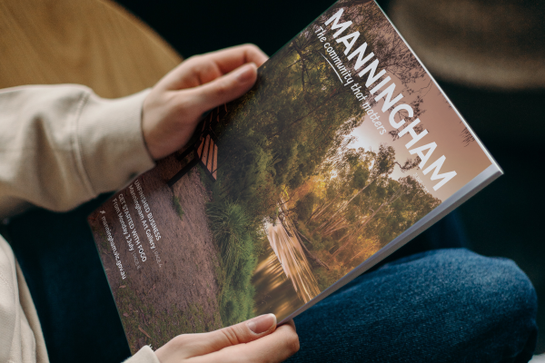 A pair of hands holding a magazine with a beautiful riverside landscape on the cover and the words 'Manningham. The community that matters.'