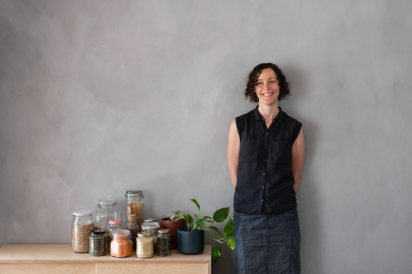 A woman with short, curly hair smiles next to glass jars of bulk foods