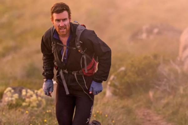 A man dressed in black and wearing a backpack and gloves runs up a mountain path