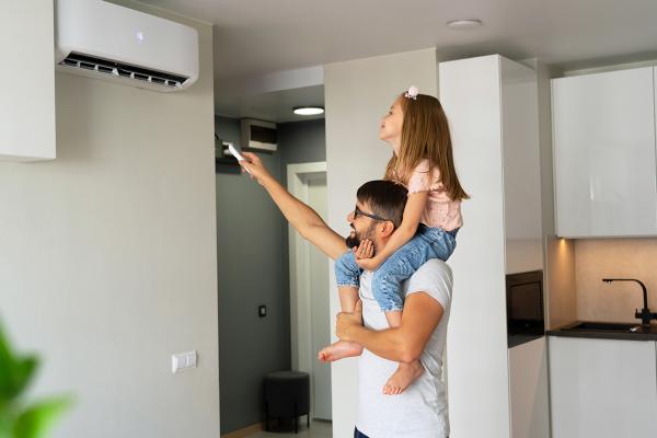 Father with little daughter on shoulders turn on reverse cycle air conditioner using remote control