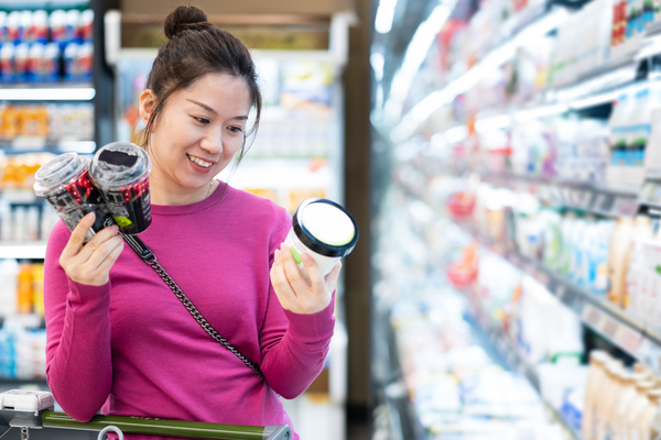 Woman in purple top comparing food labels in supermarket aisle 