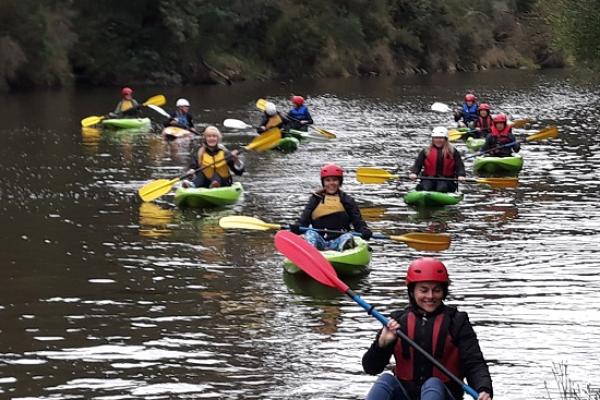 Women paddling canoes down a river wearing helmets and life jackets