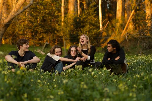 Members of the band BOTH sitting in a field of grass and yellow flowers with bushland in the background.
