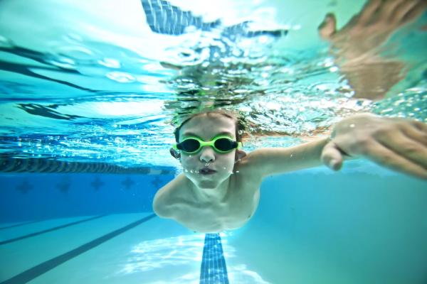 A young boy with goggles on swimming underwater in a large swimming pool