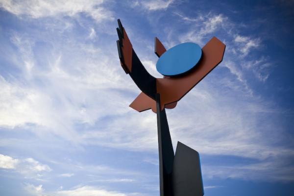 Large steel sculpture comprising bold geometric shapes in black, brown and blue sits against a blue sky.