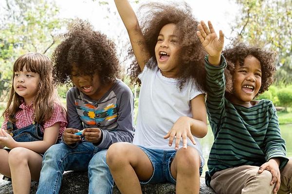 four kids sitting on a rock holding up their hands to answer questions