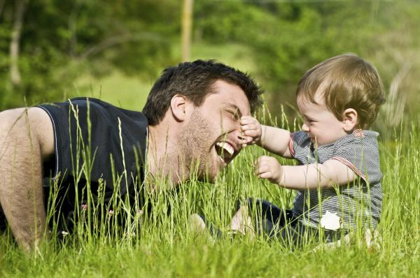 baby and dad playing in grass, baby is grabbing dad's nose and dad is laughing