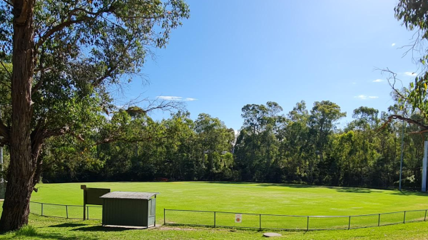 A green football oval surrounded by native trees, a small shelter in the foreground