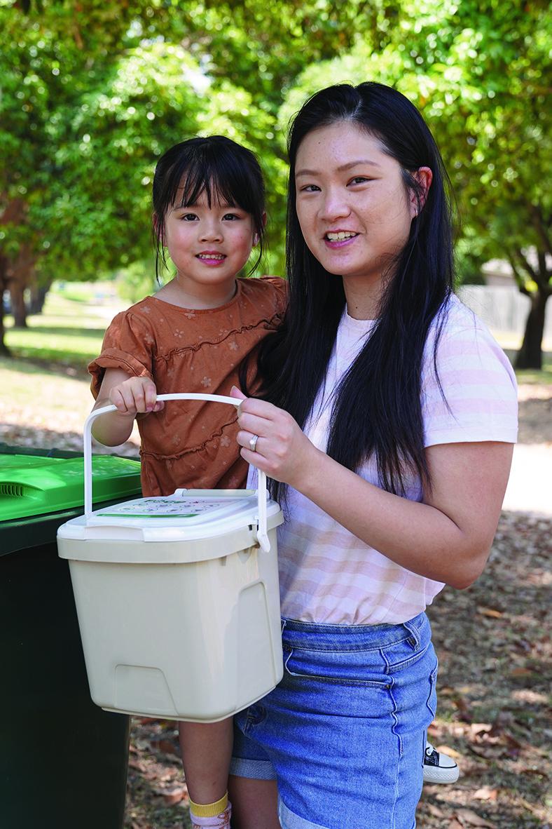 A young woman is holding a child on her hip, together they are holding a light brown FOGO caddy