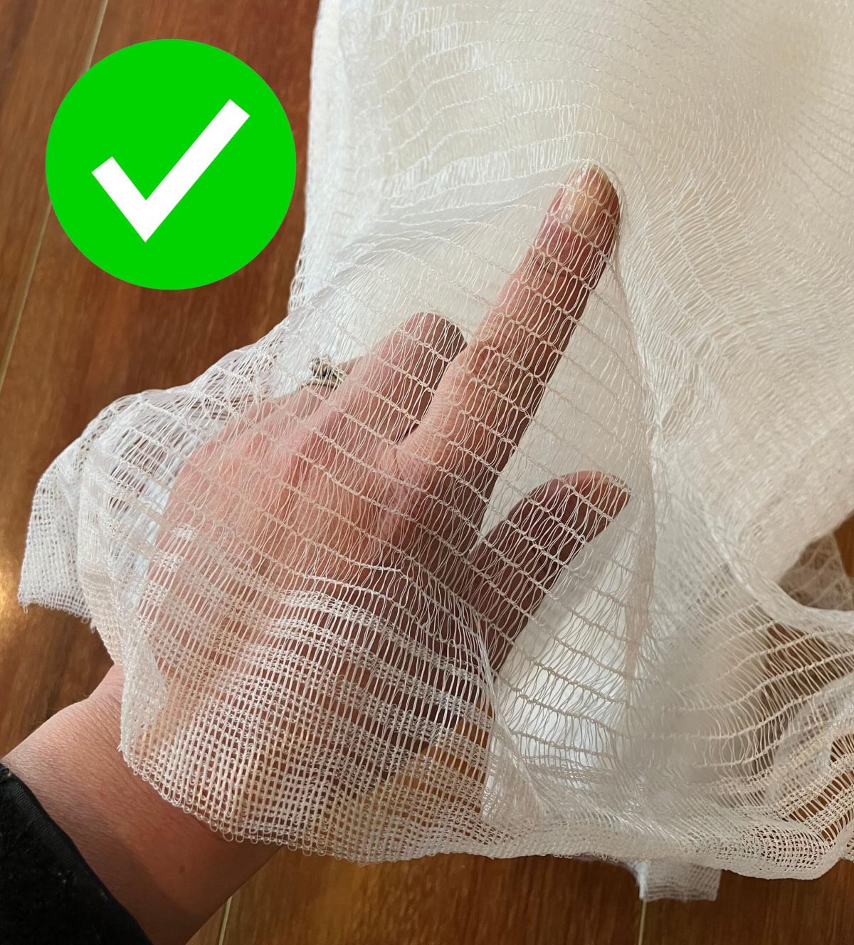 Hand with finger pointing inside a legal fruit tree net with a large green tick