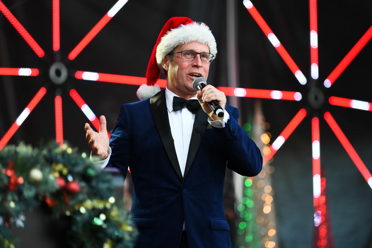 Man wearing a navy suit and Santa hat singing into a microphone on stage