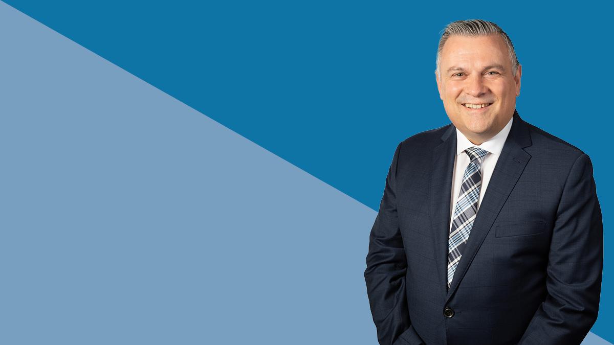 A man in a suit standing in front of a blue background