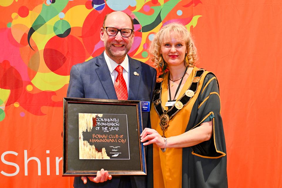 Rotary Club representative and Mayor Cr Carli Lange stand smiling in front of an orange background.