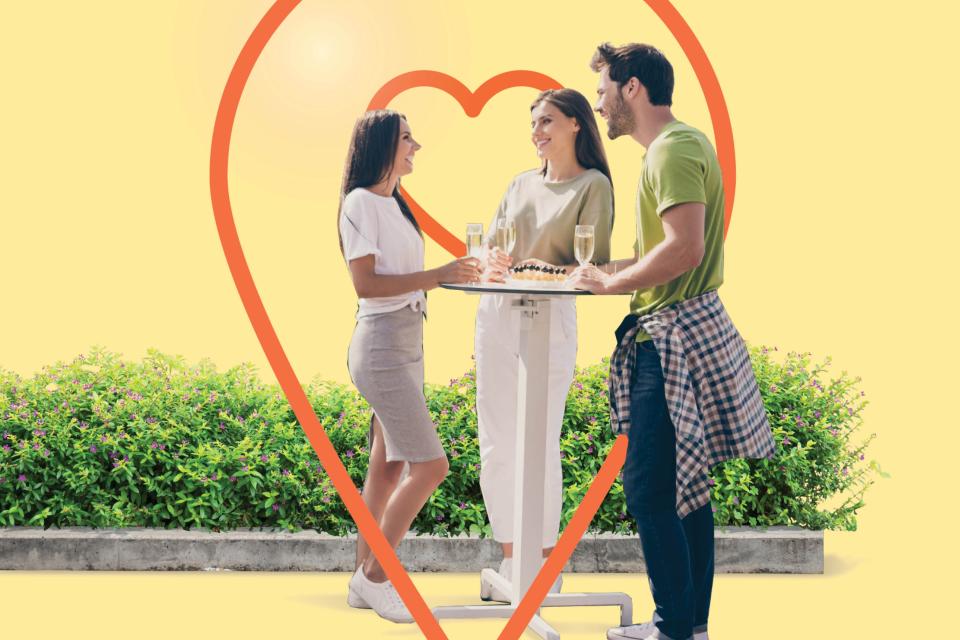 Three people stand around a raised table drinking champagne and smiling at each other