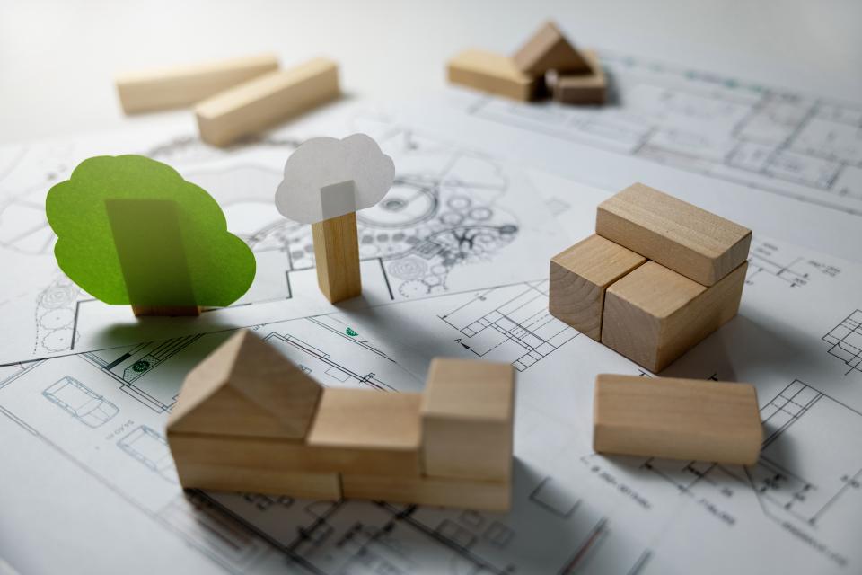 Small wooden blocks arranged in the shape of houses and paper trees sit on top of architectural drawings