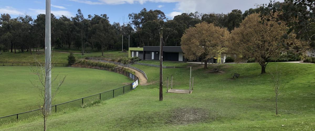 Football oval and surrounding green parkland with picnic table in foreground and club building in background