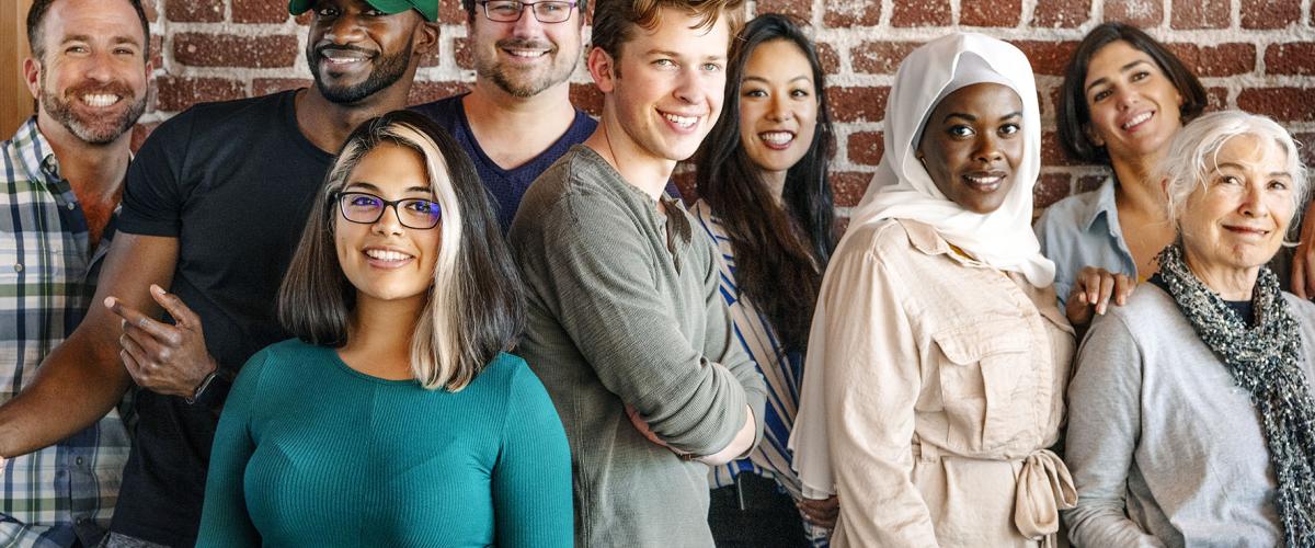 Group of people of all ages and nationalities standing against a red brick wall