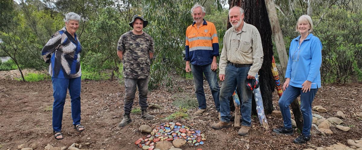 Five people in a bush setting smiling and standing around a colourful pile of rocks