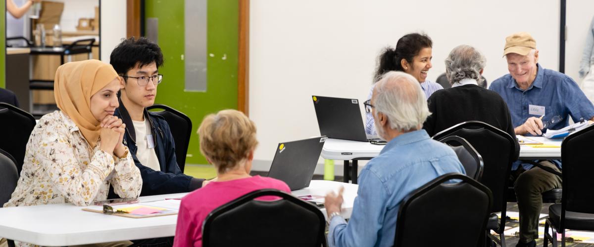 A group of people of mixed ages, ethnicities and genders sit around tables talking.