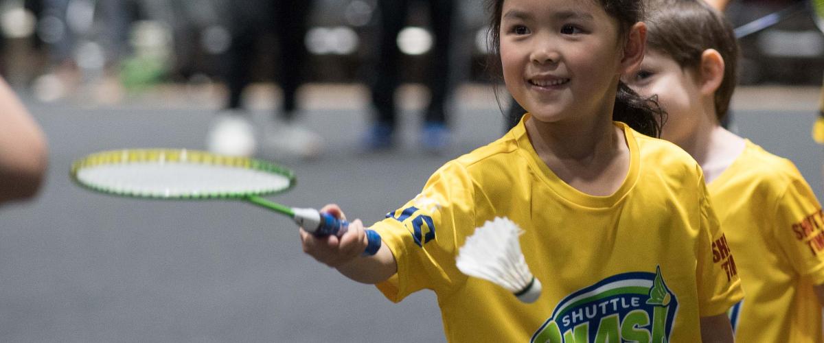 A young girl participating in Shuttle Smash Badminton wearing a yellow t-shirt