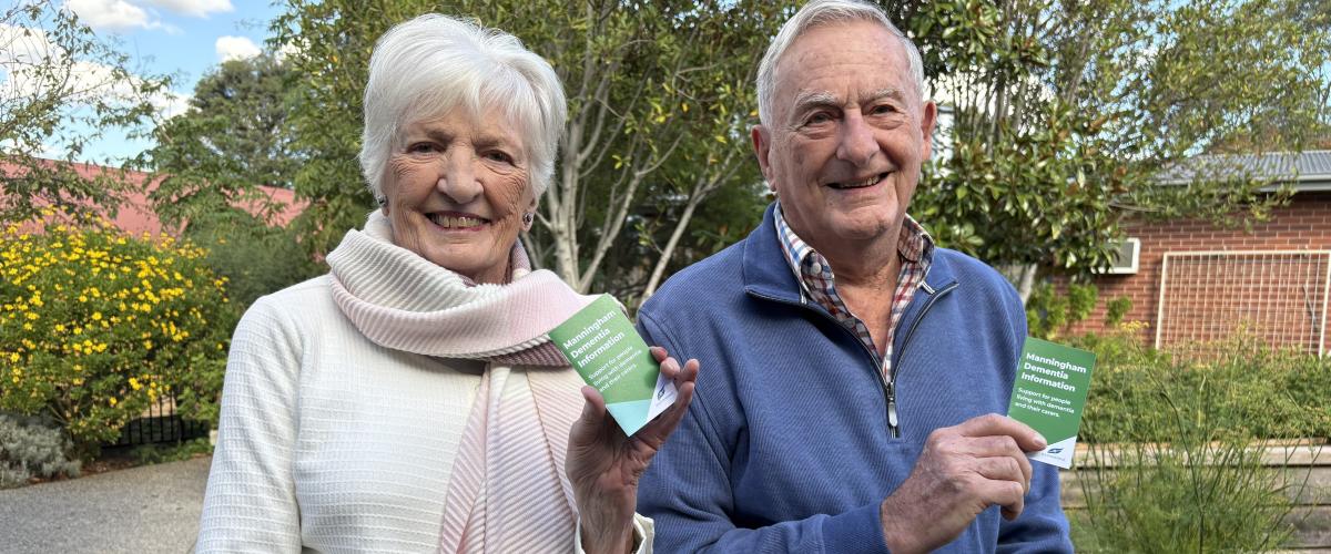 Margaret and Alan Ellery sitting in a garden holding up copies of the Manningham Dementia Information pocket guide