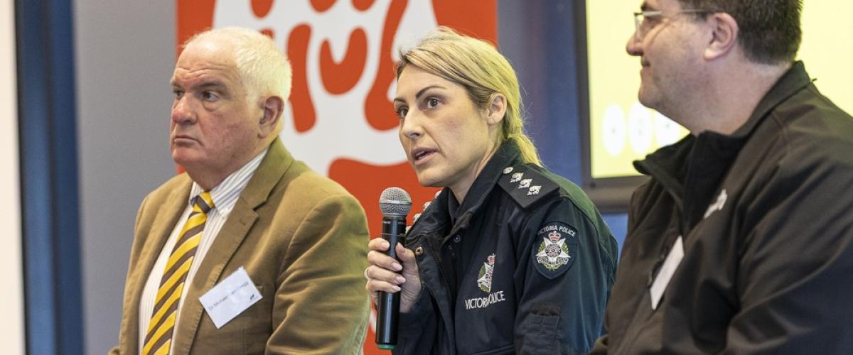 3 people sit on stage including Victoria Police member who speaks into a microphone