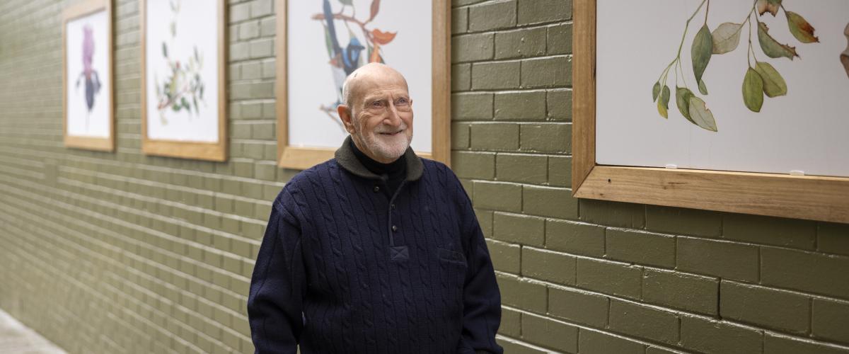 Artist Terry Napier walks down the Tunstall Square laneway which is flanked by brick walls painted a sage green which feature images of his paintings in frames.