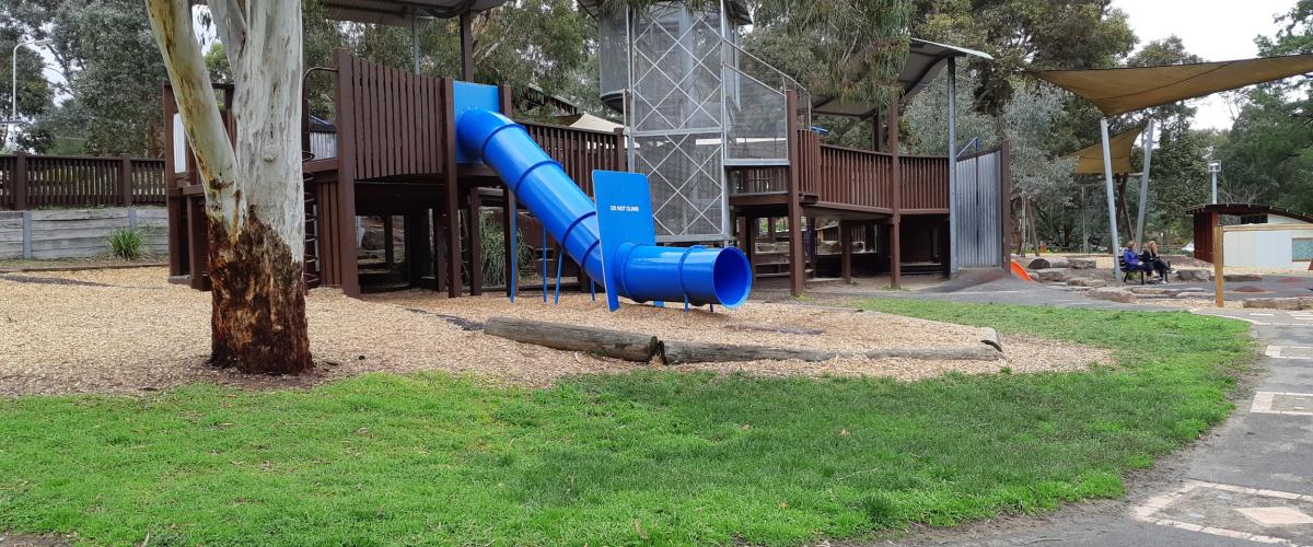 Wooden play structure with enclosed blue slide surrounded by gum trees