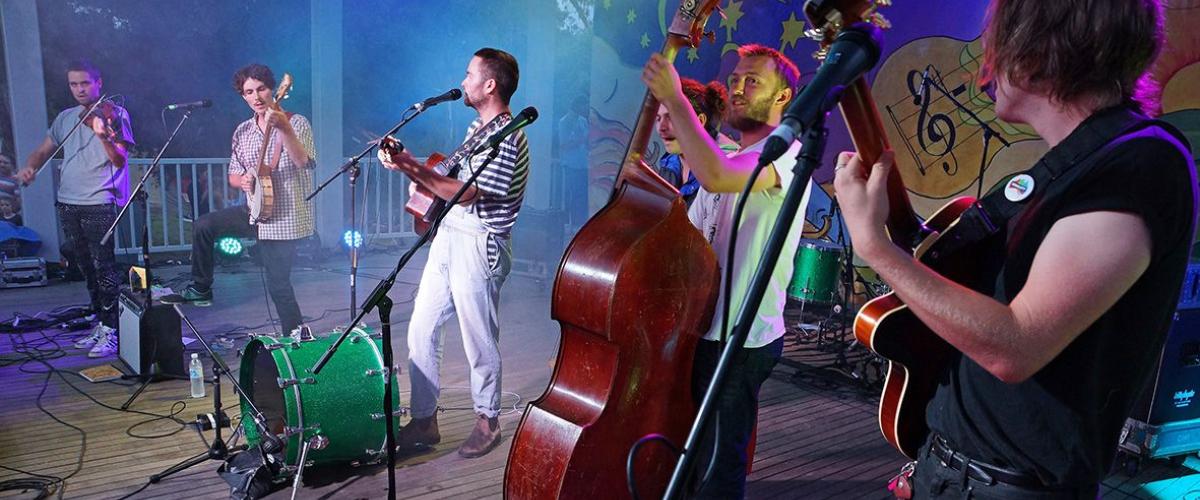 Five band members playing instruments on a stage under blue lighting