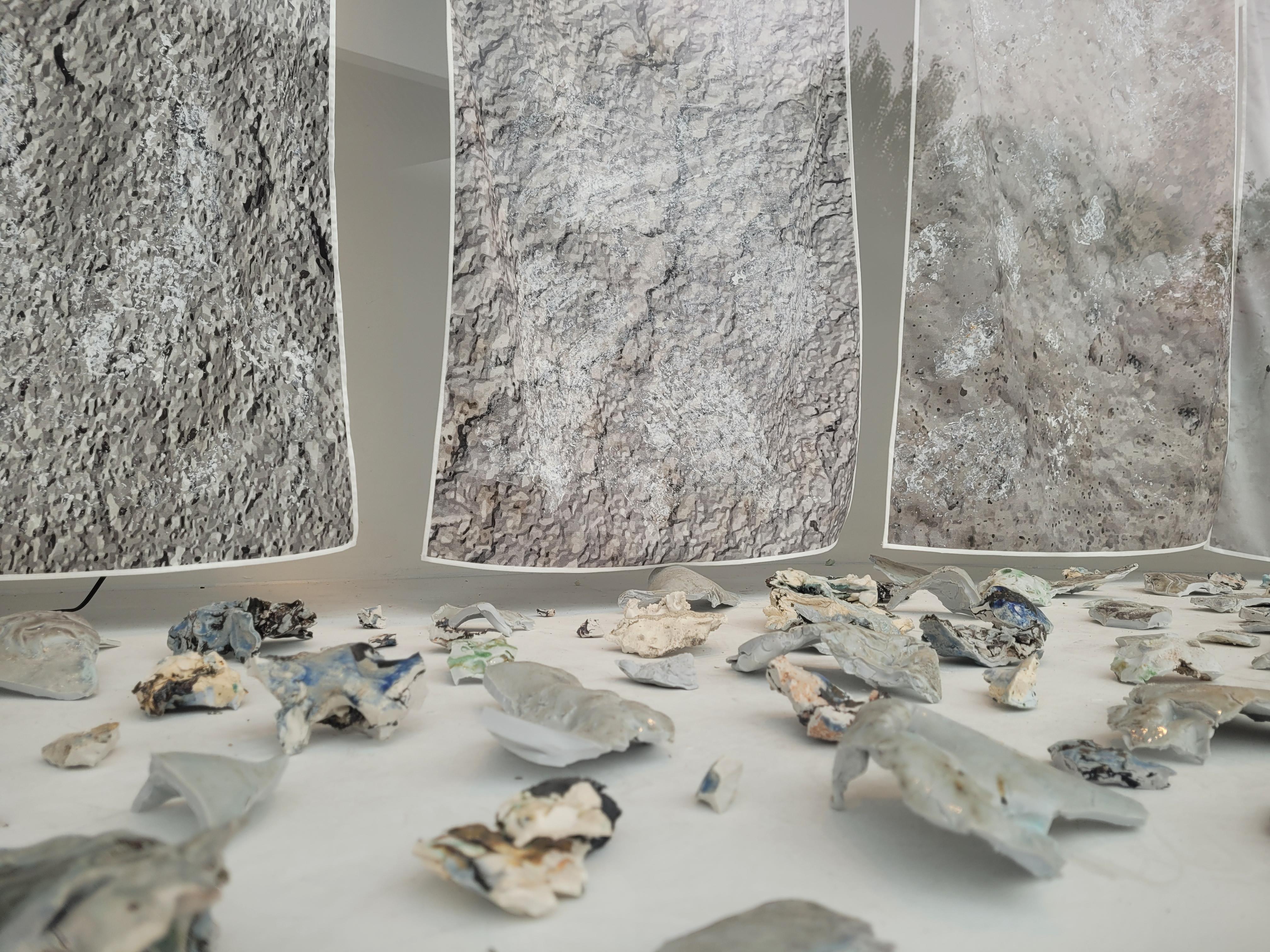 Photograph of a display in Manningham Art Gallery's Curio window space featuring amorphous ceramic items in the foreground and silk prints in the background.