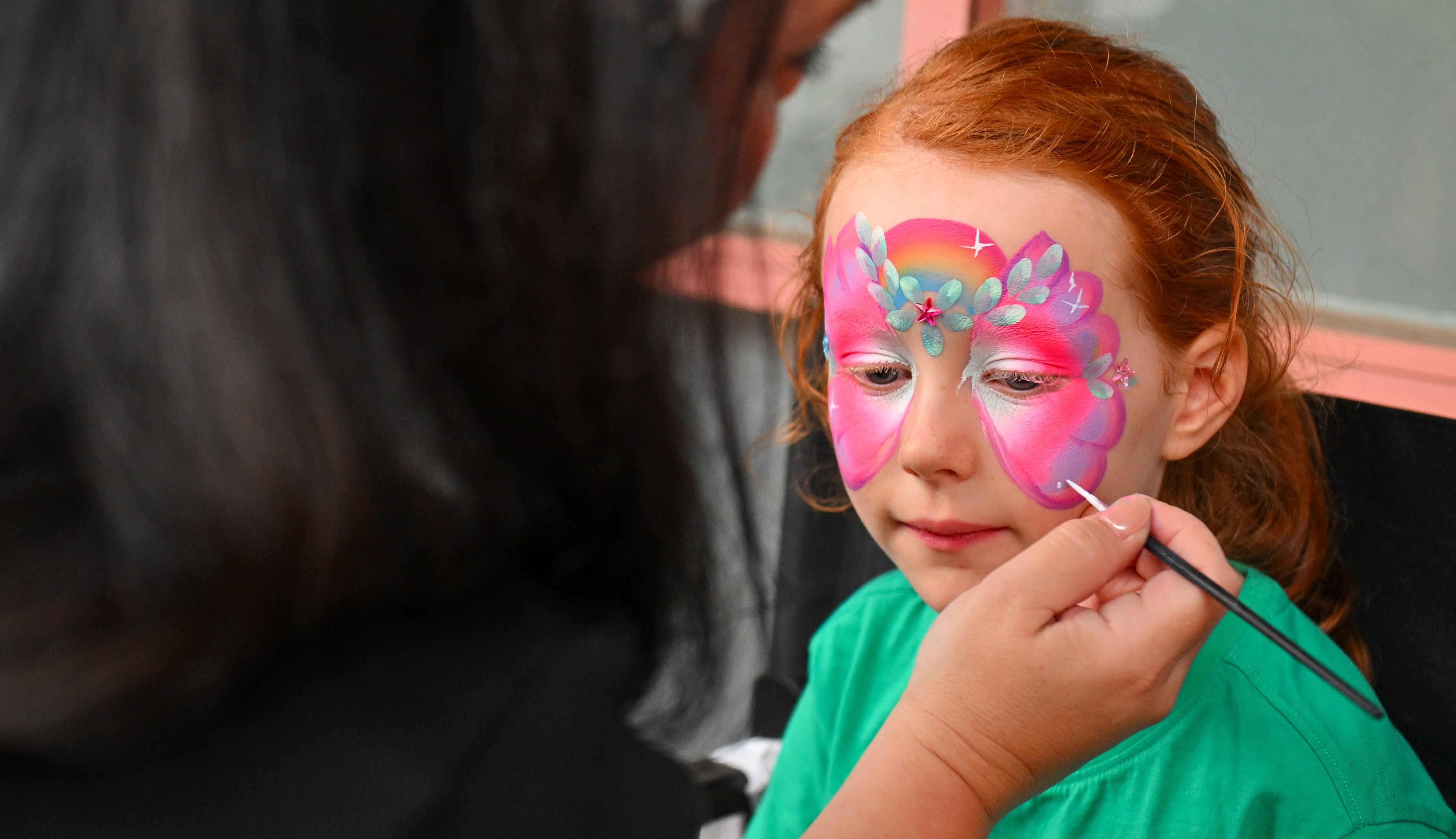 Girl having her face painted like a butterfly in pink. 