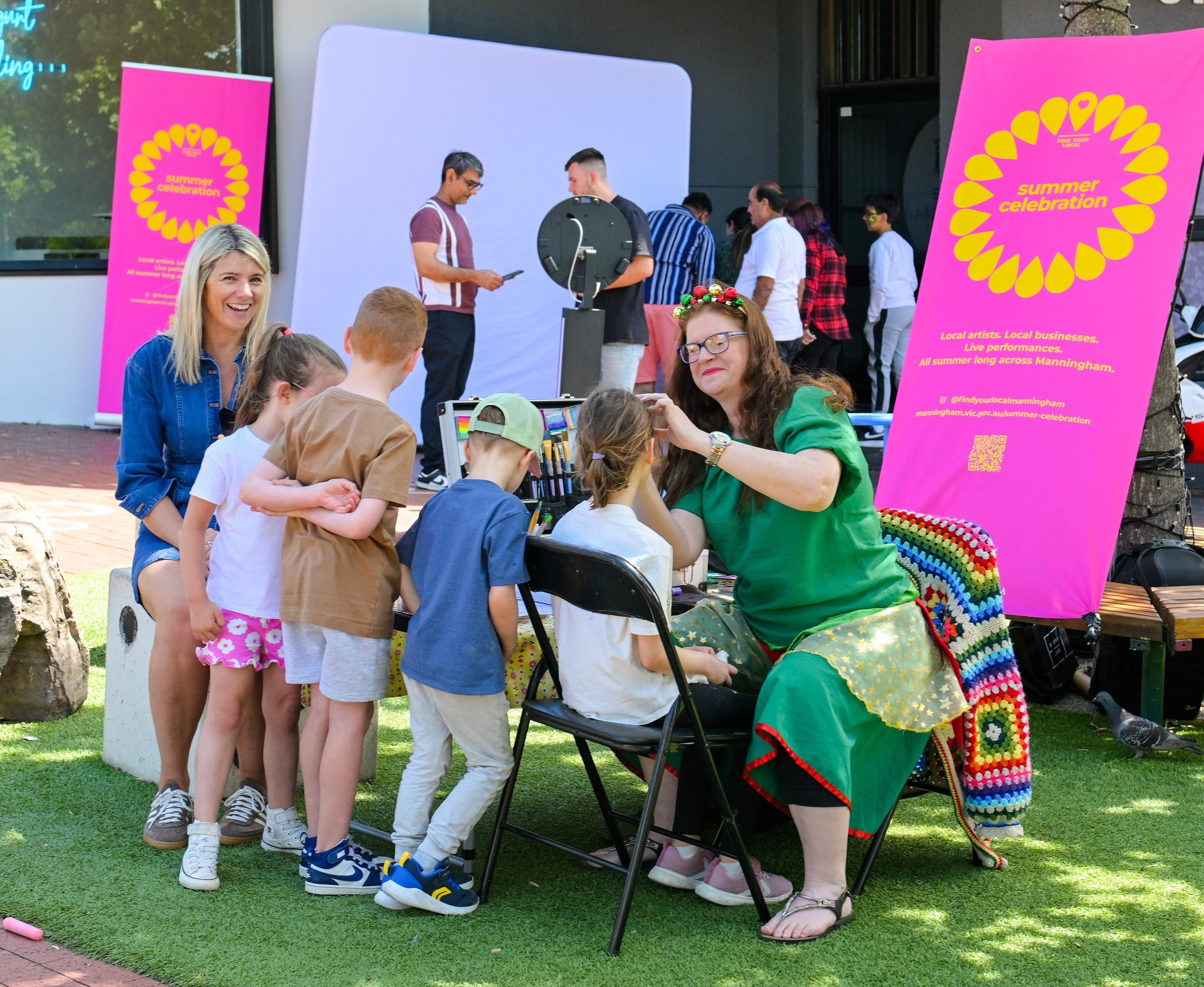 Group of kids having their faces painted and adults chatting in the background 