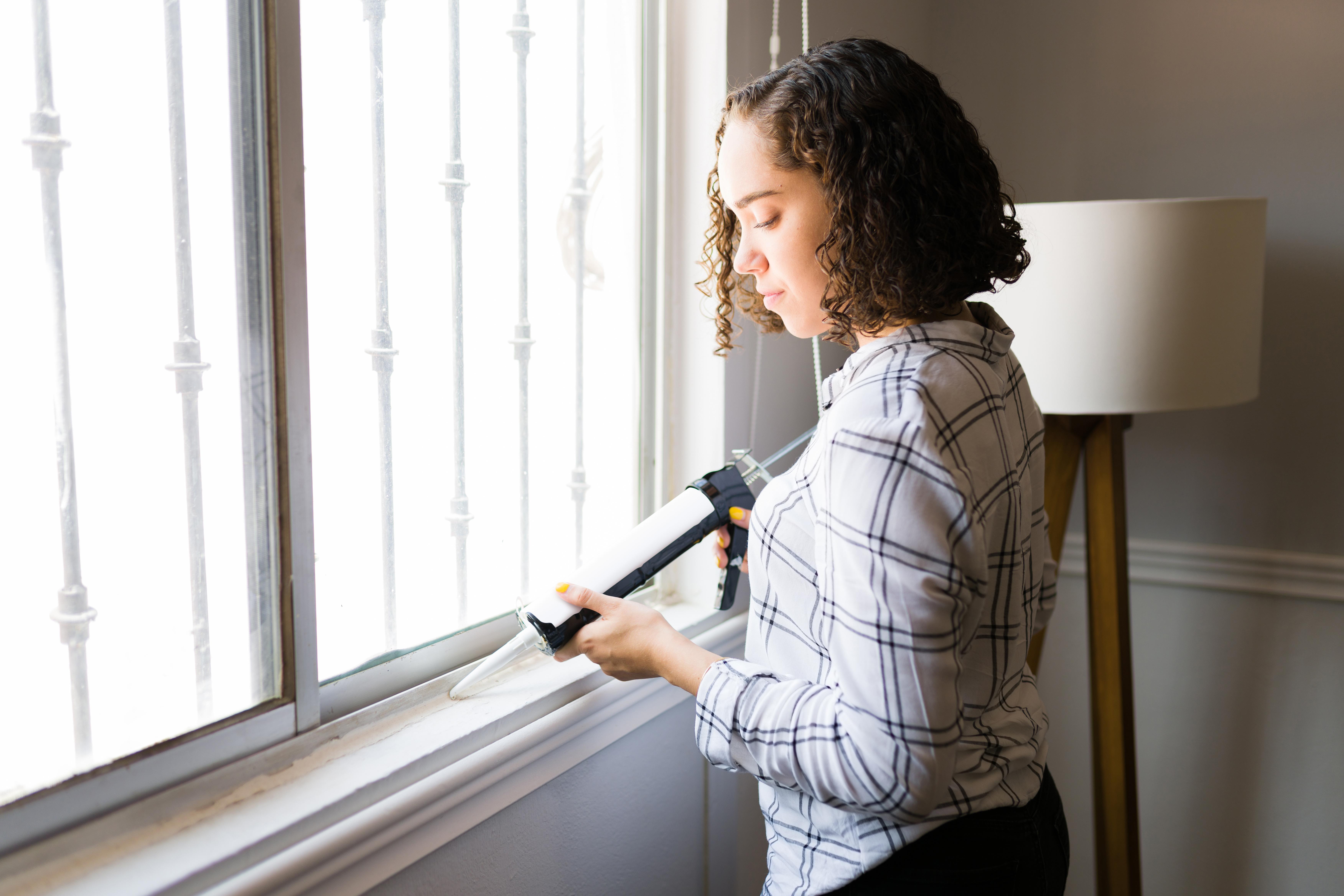 A woman applying caulking compound to weather seal a window