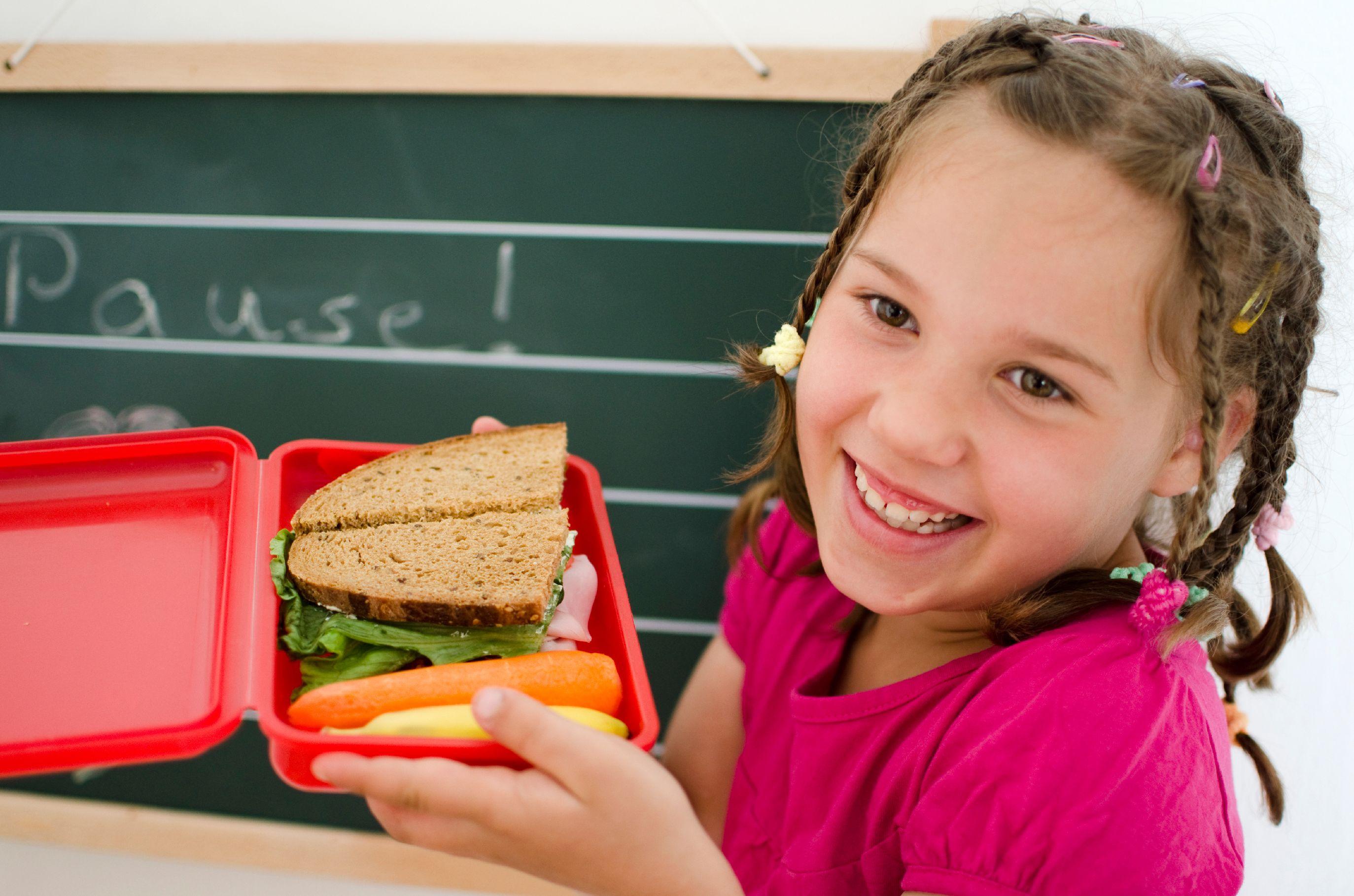 Young girl holding a lunch box with sandwich and carrots 