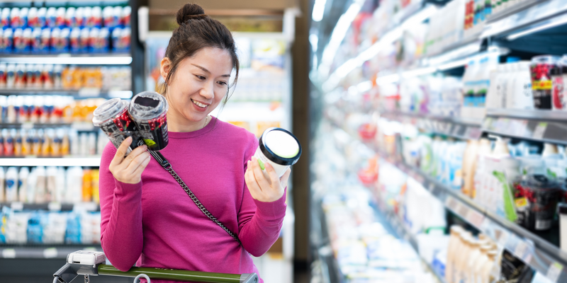 Woman in purple top comparing food labels in supermarket aisle 