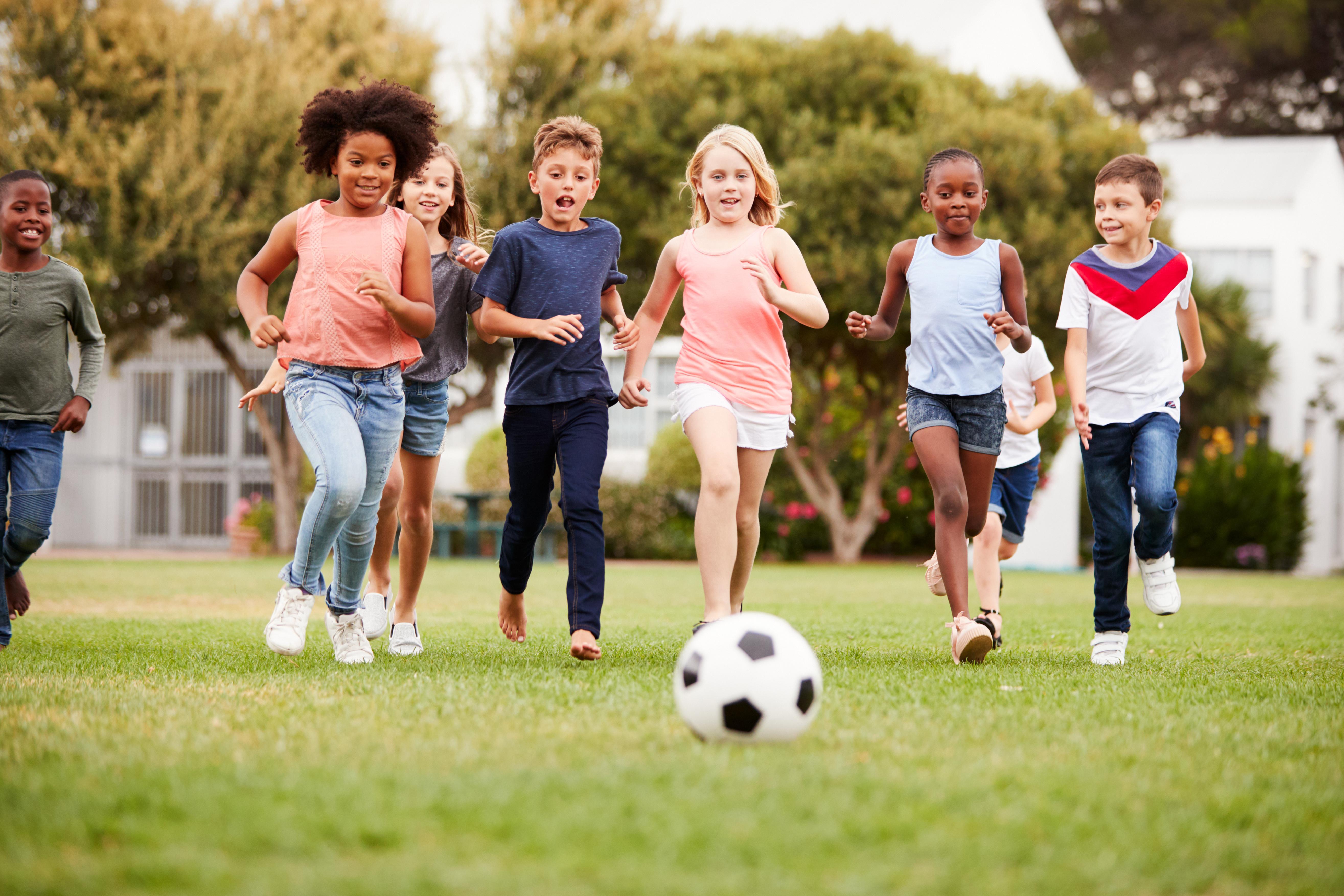 Seven children running after a soccer ball in the park