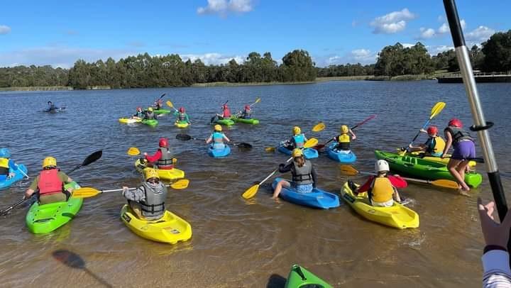 Young children paddling on yellow, green and blue canoes on a river