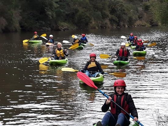 Women paddling canoes down a river wearing helmets and life jackets