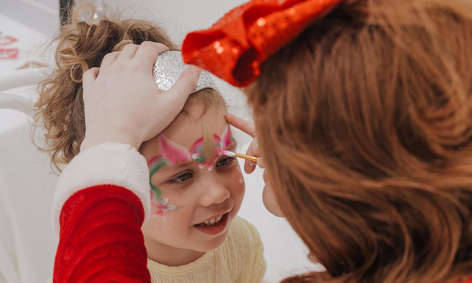 Girl having her face painted like a butterfly in pink.