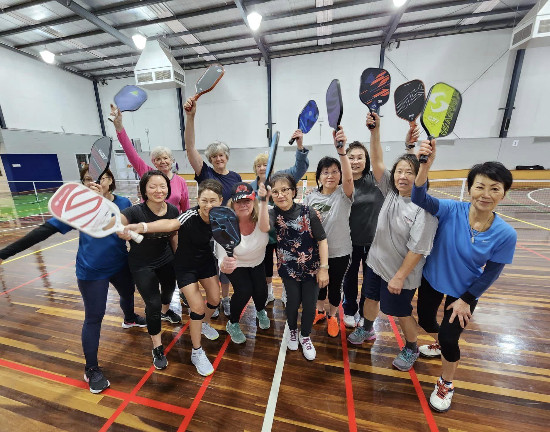 Group of women smiling holding pickleball bats in the air