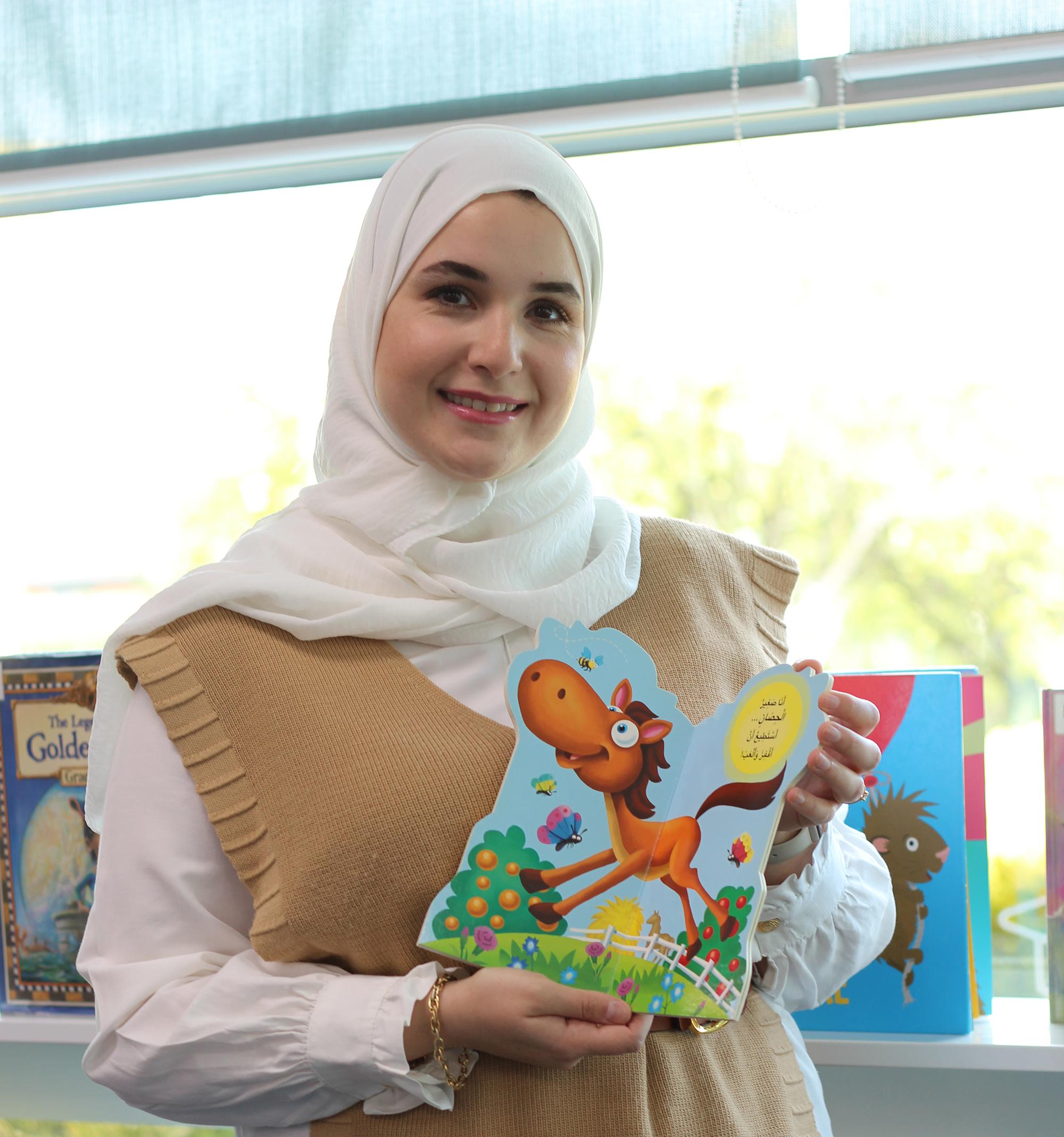 Smiling Arabic woman holding picture book open to page with cartoon horse