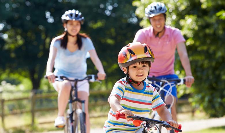 photo of child riding bicycle in front of his parents who are also riding bicycles