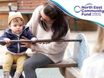 A woman and toddler sit on one end of a seesaw. The woman is holding the boy and looking down at him.