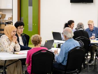 A group of people of mixed ages, ethnicities and genders sit around tables talking.