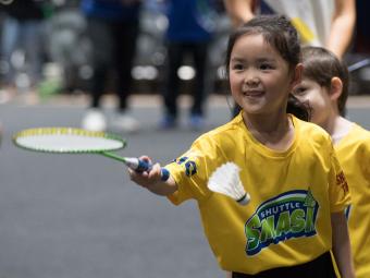 A young girl participating in Shuttle Smash Badminton wearing a yellow t-shirt