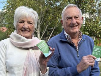 Margaret and Alan Ellery sitting in a garden holding up copies of the Manningham Dementia Information pocket guide