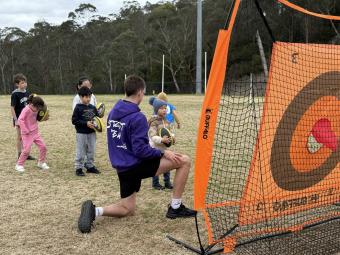 Young children lining up on an oval to throw a football through a target.