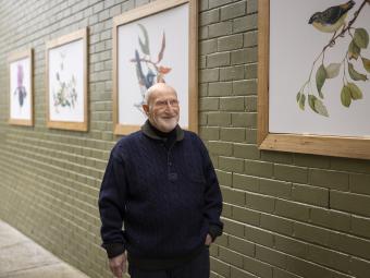 Artist Terry Napier walks down the Tunstall Square laneway which is flanked by brick walls painted a sage green which feature images of his paintings in frames.