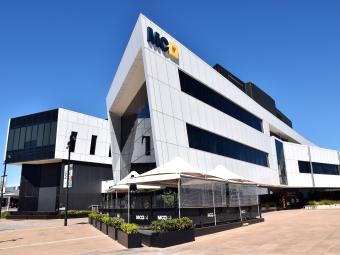 A large modern white and black angular building with a cafe on the ground level and a tiled forecourt. 